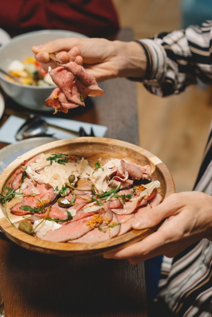 pexels-photo-6954476 A close-up of sliced meat garnished with herbs, served on a wooden tray.